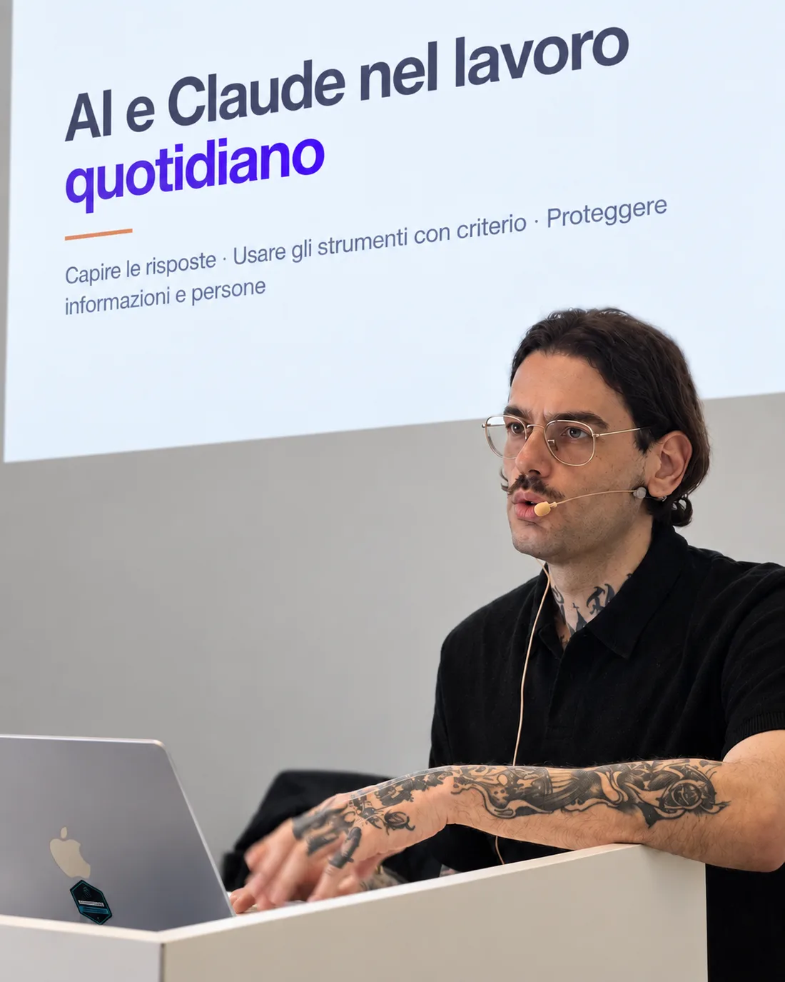 Giovanni Liguori in aula al leggio, con microfono ad archetto e computer portatile, davanti alla slide «AI e Claude nel lavoro quotidiano».